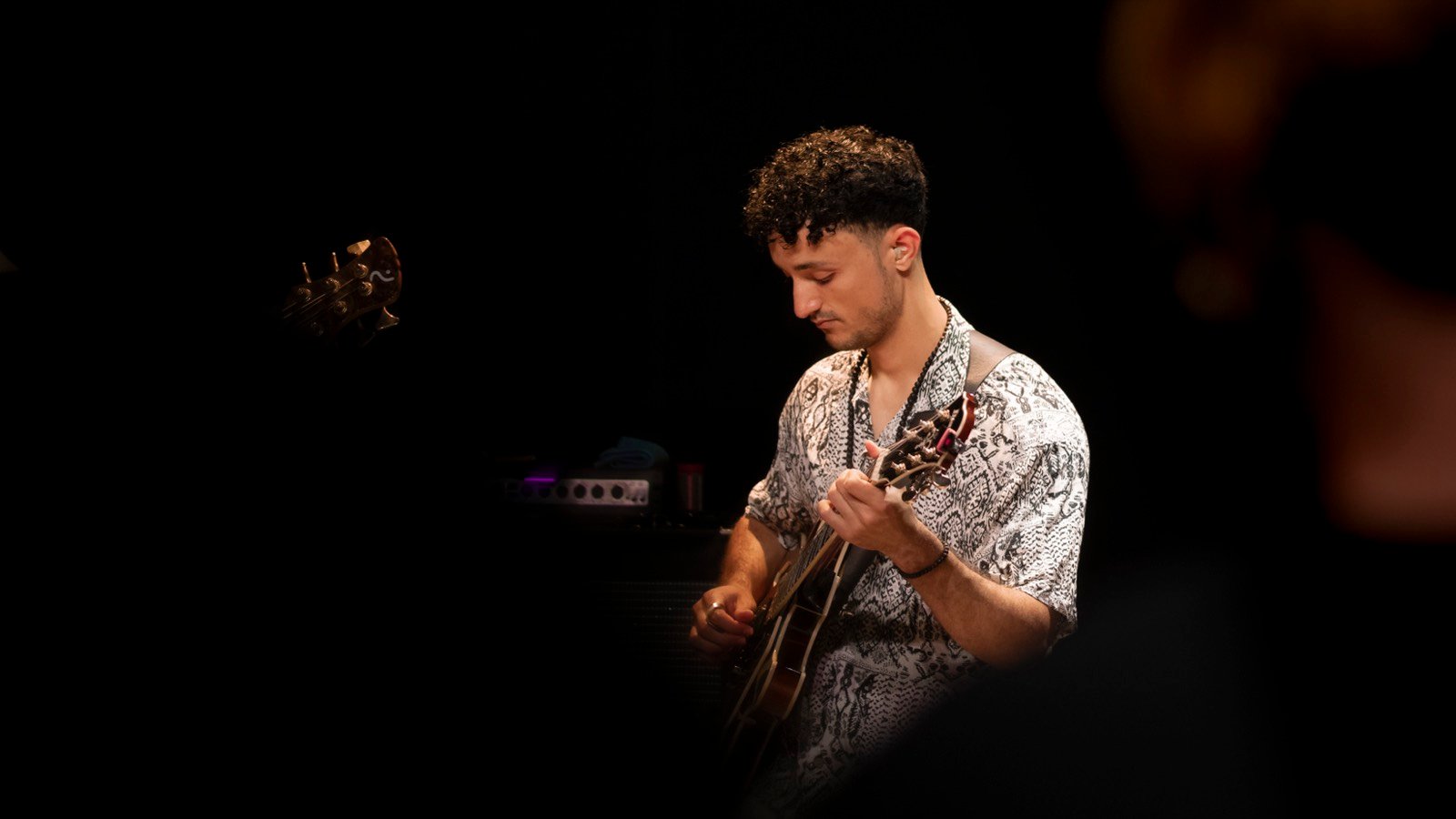 Lucas Baret playing the hollowbody archtop, eyes down on the fretboard, under warm light on a dark stage