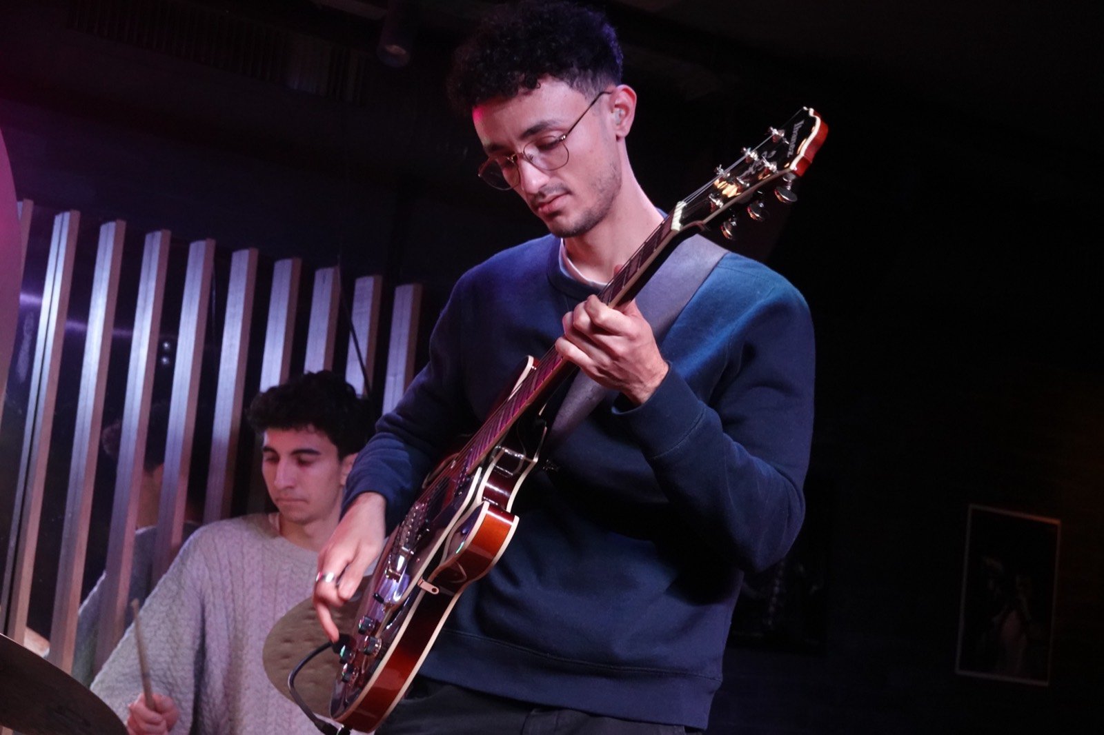 Lucas Baret playing the archtop in a low-lit club, a drummer behind him