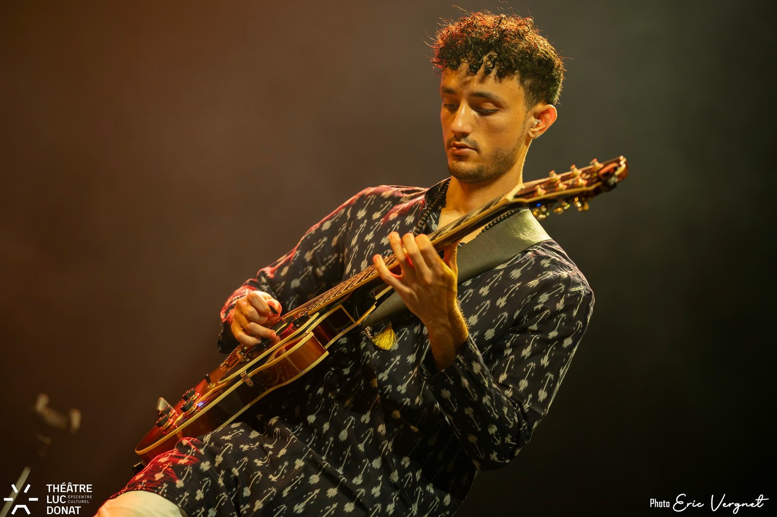 Lucas Baret playing a hollowbody archtop guitar under warm stage light, eyes down on the fretboard